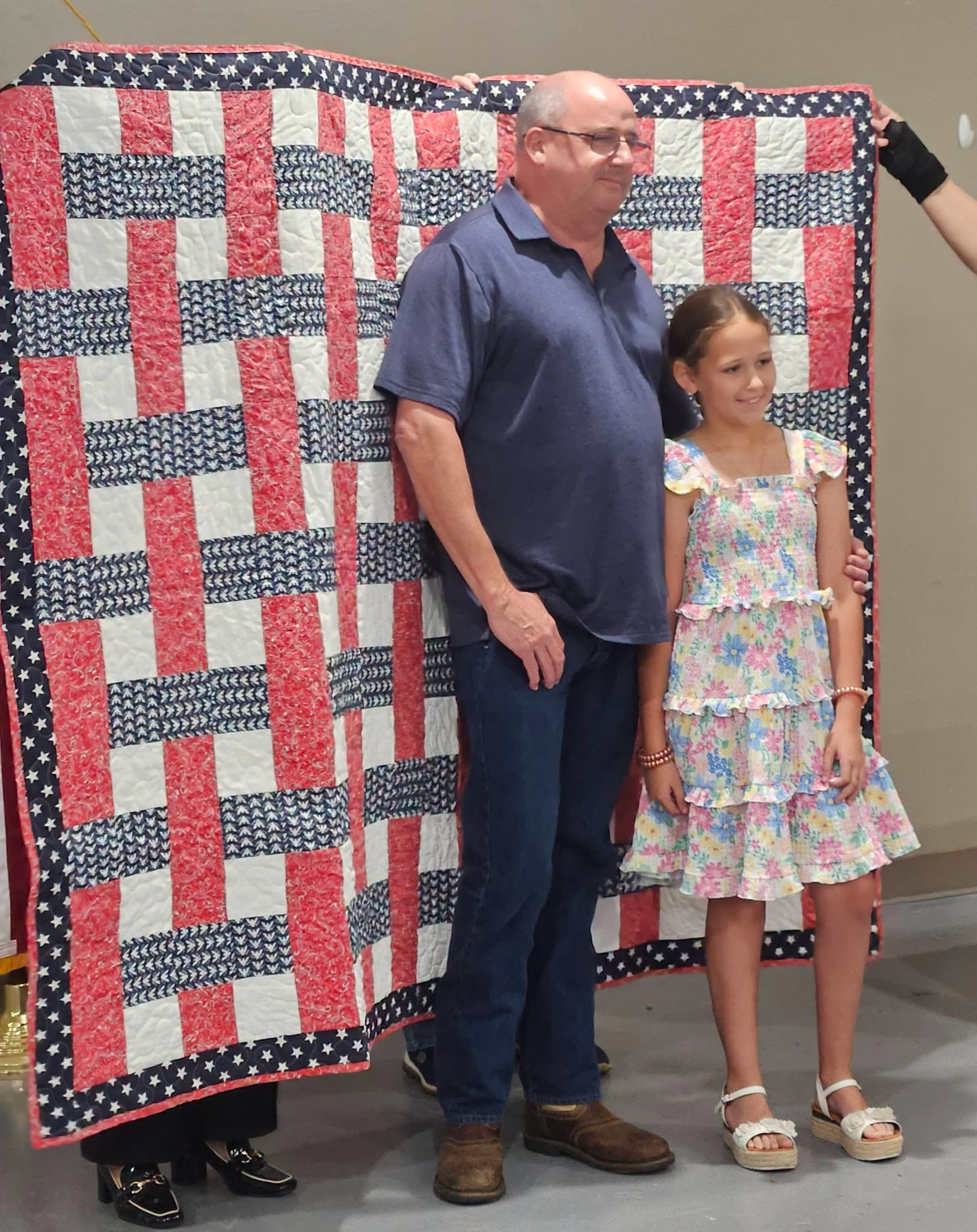 man and girl standing in front of red, white, and blue quilt